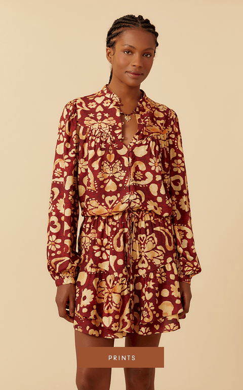 A model with short black hair styled back in a casual look, wearing a black jumpsuit with side pockets and black sandals with silver details. The model is posing against a white background in a category banner with the word 'Monochromatic' in white text on a brown background.