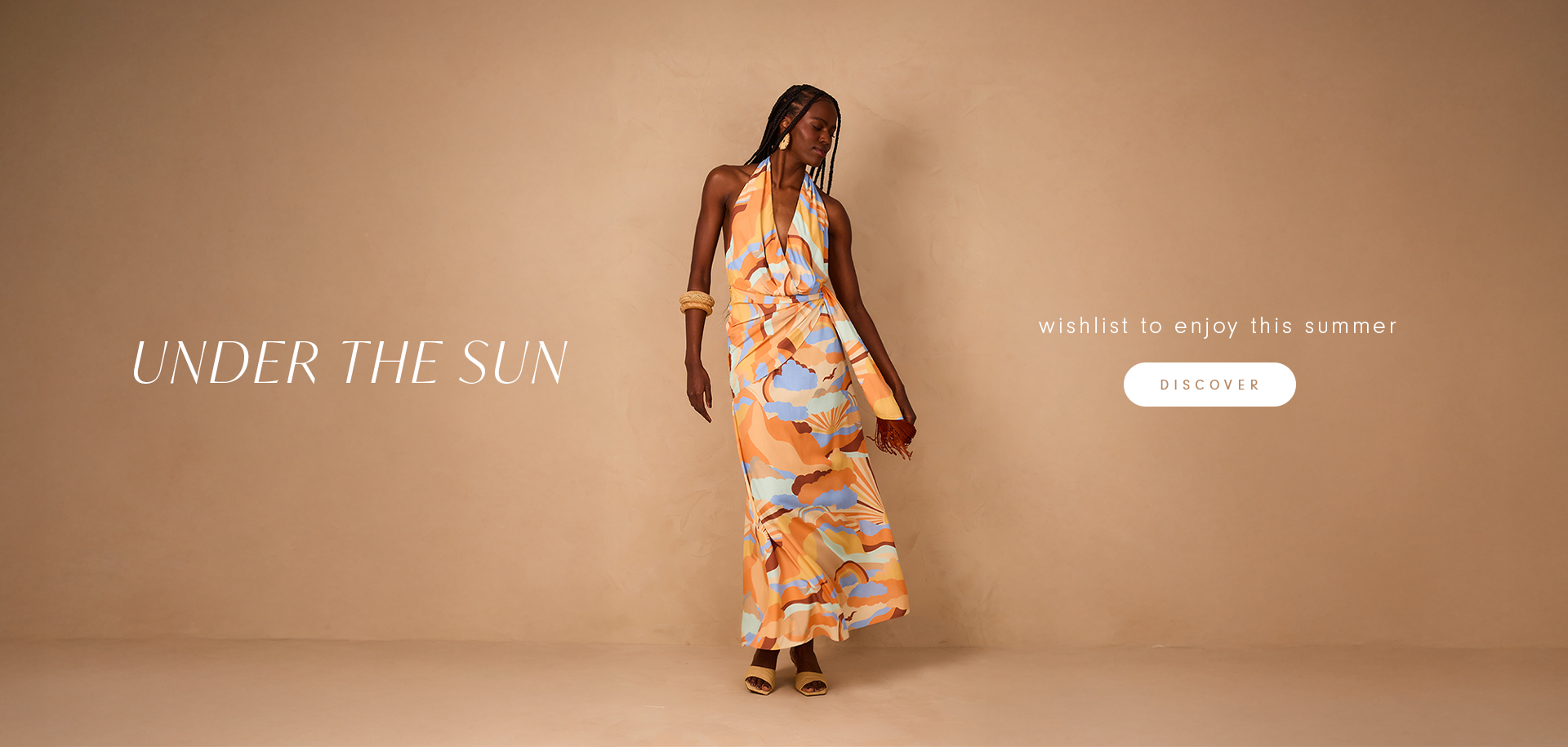Black woman with long braids wearing a colorful printed halter dress in shades of orange, blue, and white, standing in front of a beige background. Text: “UNDER THE SUN.” Caption: “wishlist to enjoy this summer.” Button: “DISCOVER.”