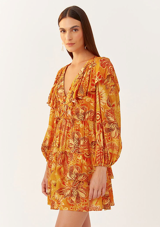  A brunette model is wearing a short, long-sleeve dress with puffed sleeves, printed in orange and caramel.