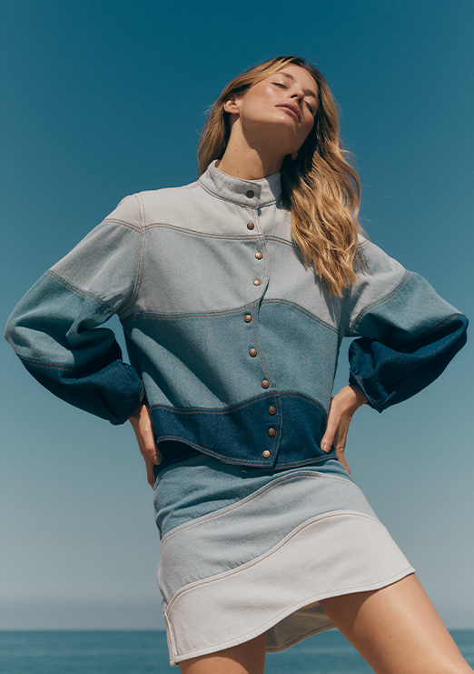 The model is wearing a denim set from Dress To’s winter collection, featuring a long-sleeved jacket and a short skirt in different denim washes, creating a modern and stylish look.