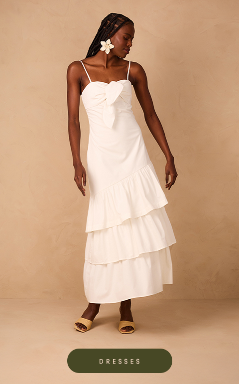 Woman wearing a sleeveless, color-blocked maxi dress in black and white with wavy trim along the chest. She stands against a neutral beige backdrop, styled with black lace-up sandals.