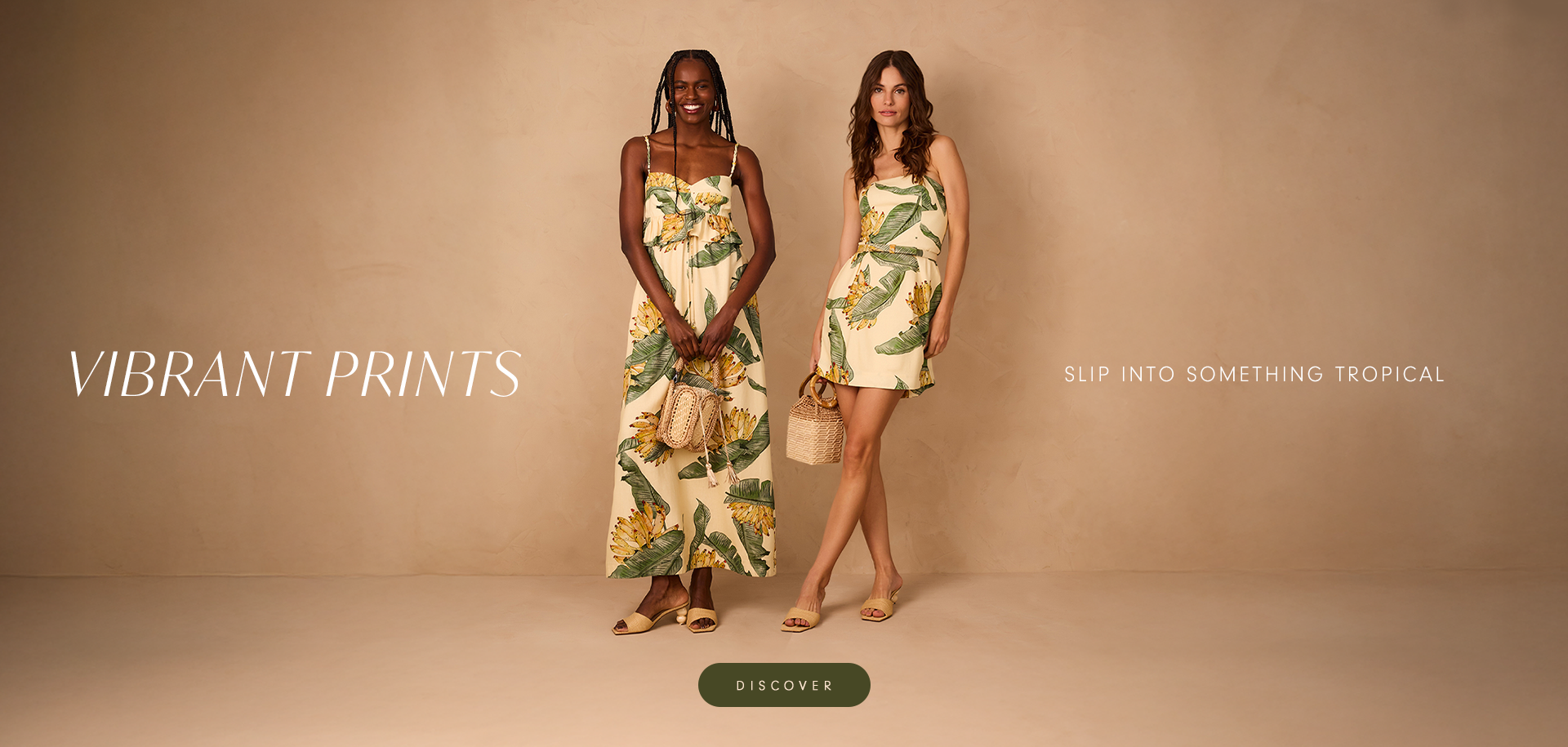 Two women wearing tropical-print dresses with green leaves and yellow flowers, standing against a warm beige background. One wears a long flowy dress, the other a short dress with a woven handbag. Text reads: 'Vibrant Prints – Slip into something tropical.' A button below says 'Discover'.