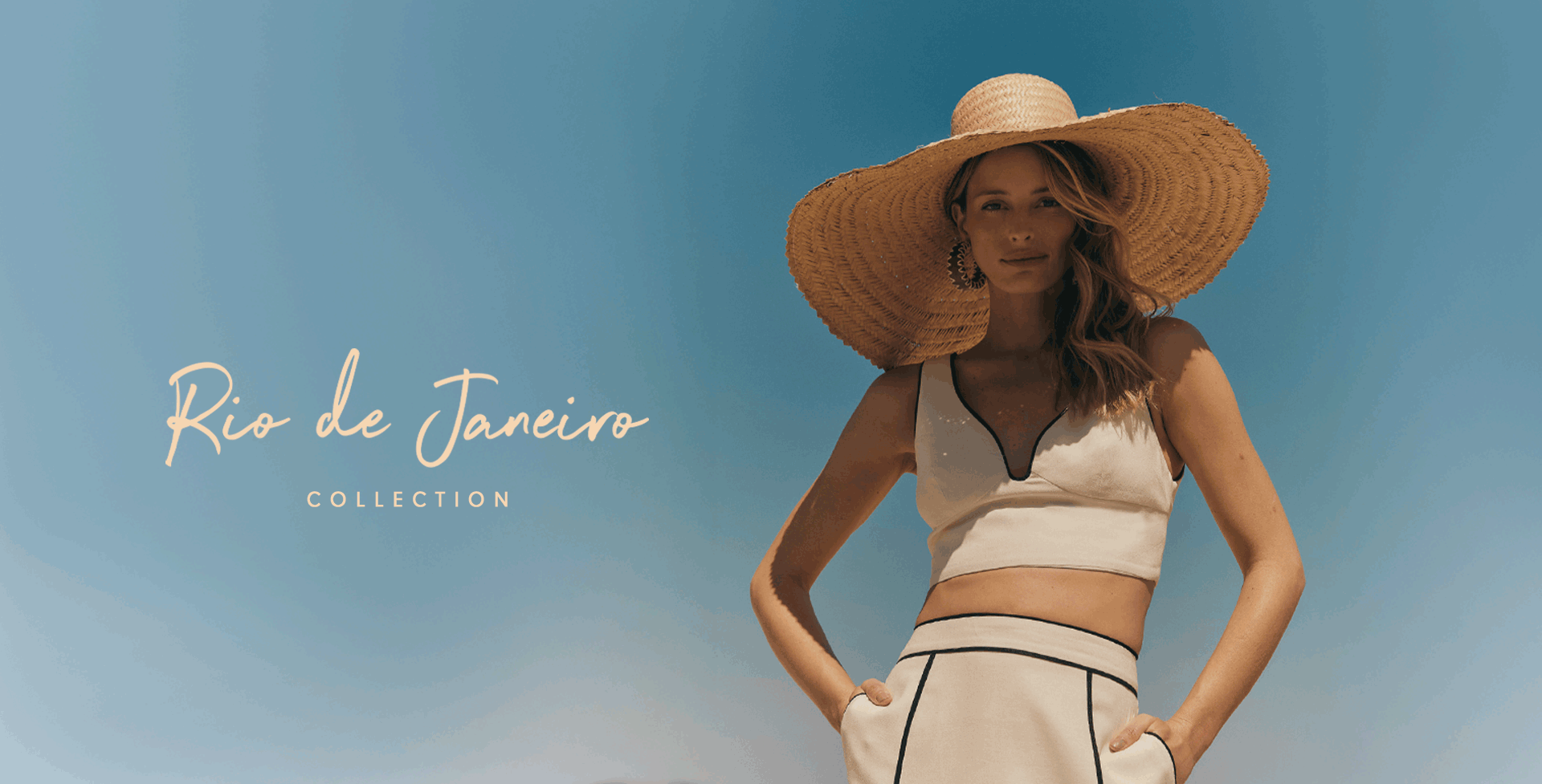 A woman poses under the bright blue sky wearing a chic white crop top with black piping and matching high-waisted shorts. She completes the look with a wide-brimmed straw hat and hoop earrings, embodying the effortless elegance of the Dress To Winter Collection: Rio de Janeiro. The scene captures the essence of sun, style, and sophistication.