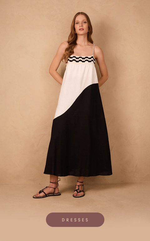 Woman wearing a sleeveless, color-blocked maxi dress in black and white with wavy trim along the chest. She stands against a neutral beige backdrop, styled with black lace-up sandals.