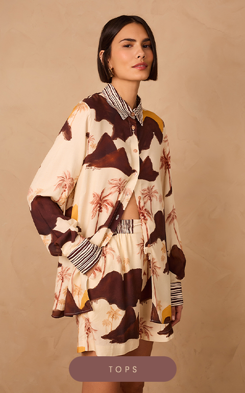 Model wearing an oversized button-up shirt from Dress To – Rio de Janeiro Collection, featuring a tropical palm tree print in shades of brown and cream, with touches of mustard yellow, and contrasting black-and-white striped cuffs and collar. She pairs it with matching elastic-waist shorts. The background is a warm beige texture. At the bottom center, there is a mauve button with white text that reads 'TOPS'.